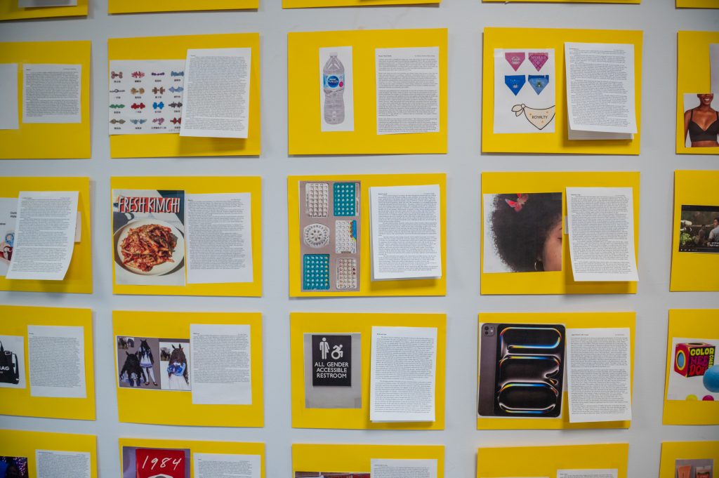 A wall display of bright yellow poster boards featuring student research projects from an Anthropology course, each containing written text, images, and artifacts exploring everyday objects and cultural practices, including topics on food, fashion, accessibility, and social norms.