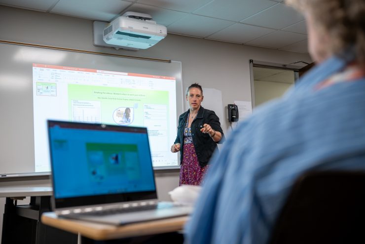Professor Carpenter leading a classroom discussion in front of a projected presentation of data. Social work student laptop open in foreground. 