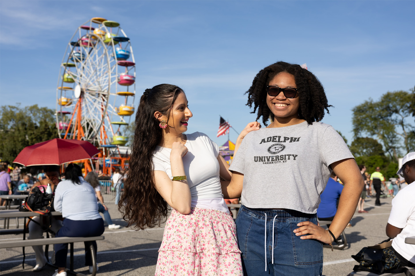 Two female Adelphi University students smile, with carnival rides in the background.