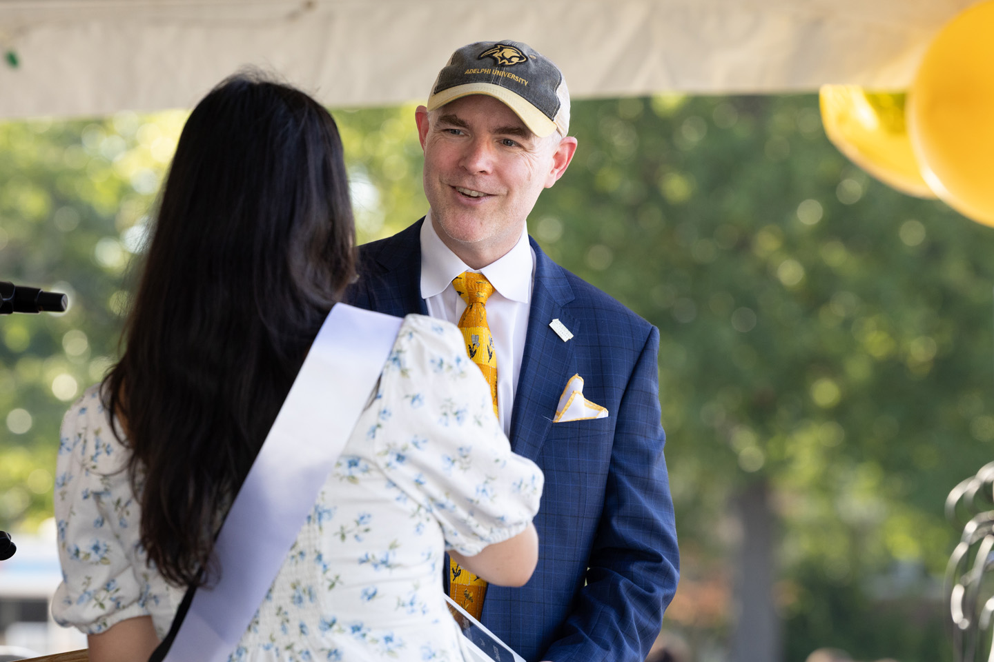Interim President Chris Storm, PhD, facing forward, chats with a woman wearing a white pageant sash.