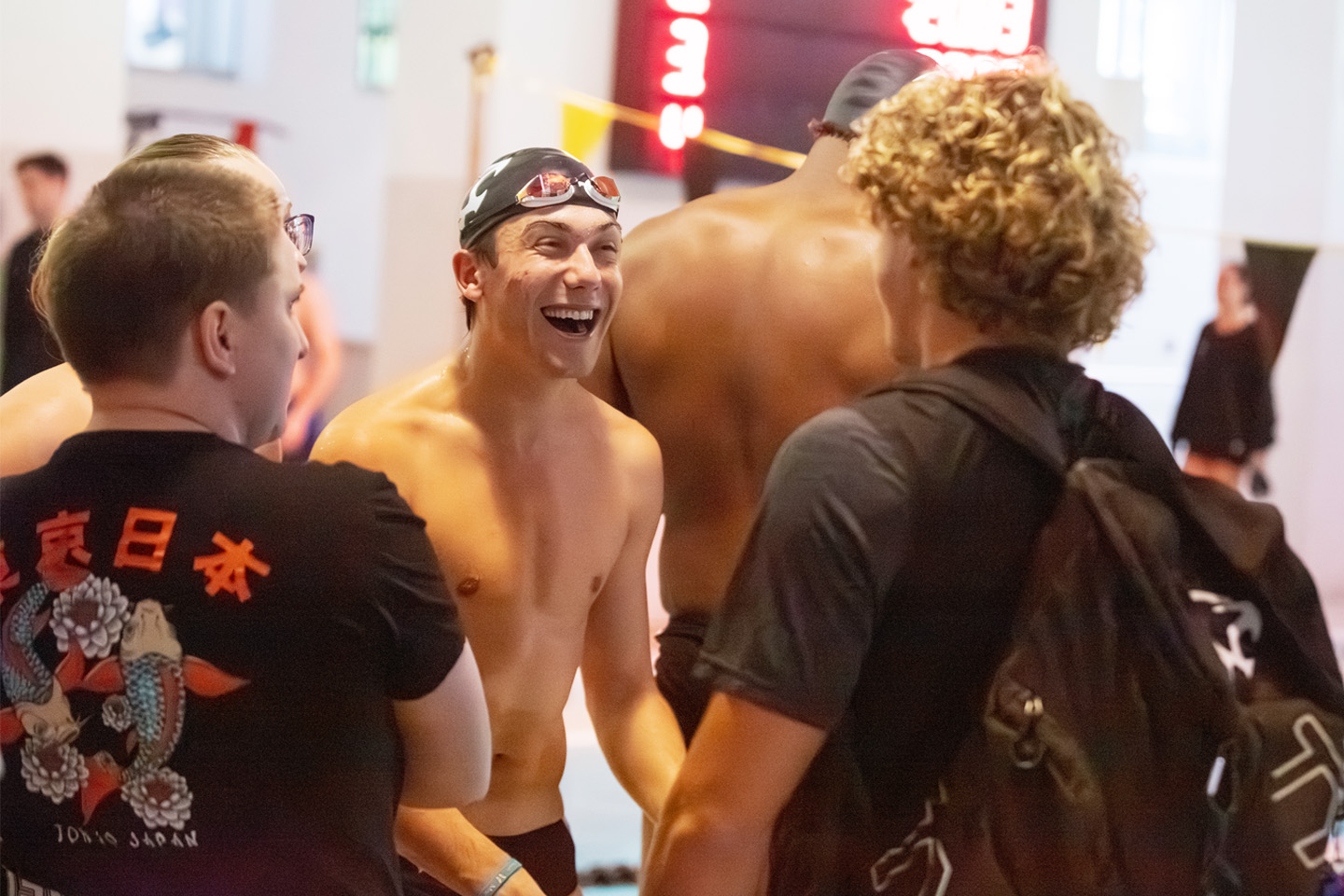 A male Adelphi swimmer smiles at two alumni in the stands.
