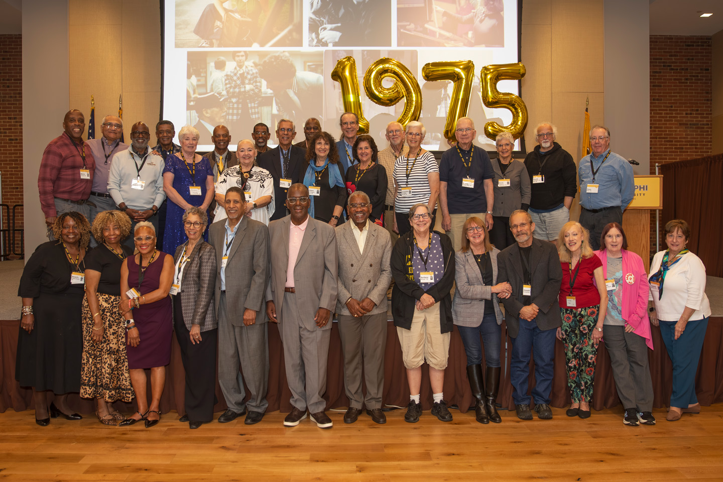 A large group of alumni stand before balloons that read “1975.”