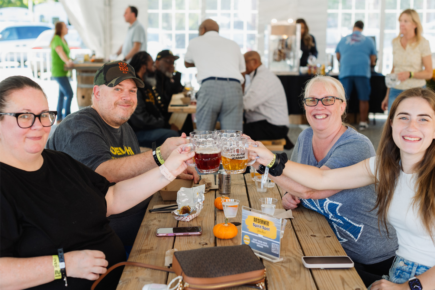 Friends sit at a wooden table, toasting with mugs of beer.
