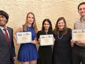 Five people posing together, four holding certificates and smiling at the camera, dressed in formal or semiformal attire.