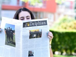 A student reads a copy of the paper on a sunny day on campus.