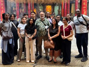 Ten Adelphi students stand in a colorful street market in Southeast Asia, with Sentwali Bakari, PhD, on far right