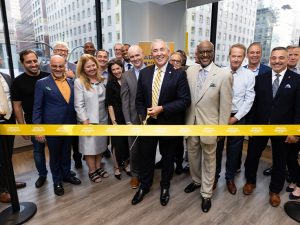 A group of people in business attire smiling at a ribbon-cutting event 