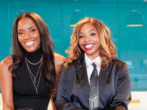 Two smiling women dressed in business attire.
