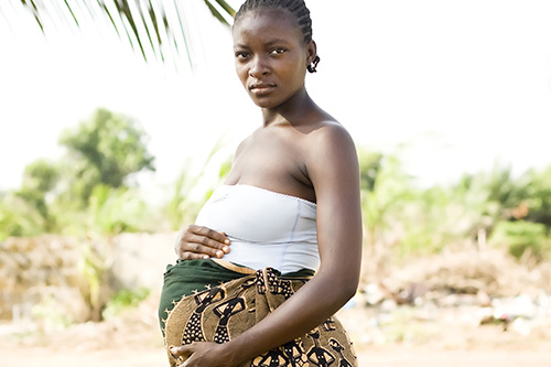 A pregnant African woman holding her stomach while looking seriously at the camera.