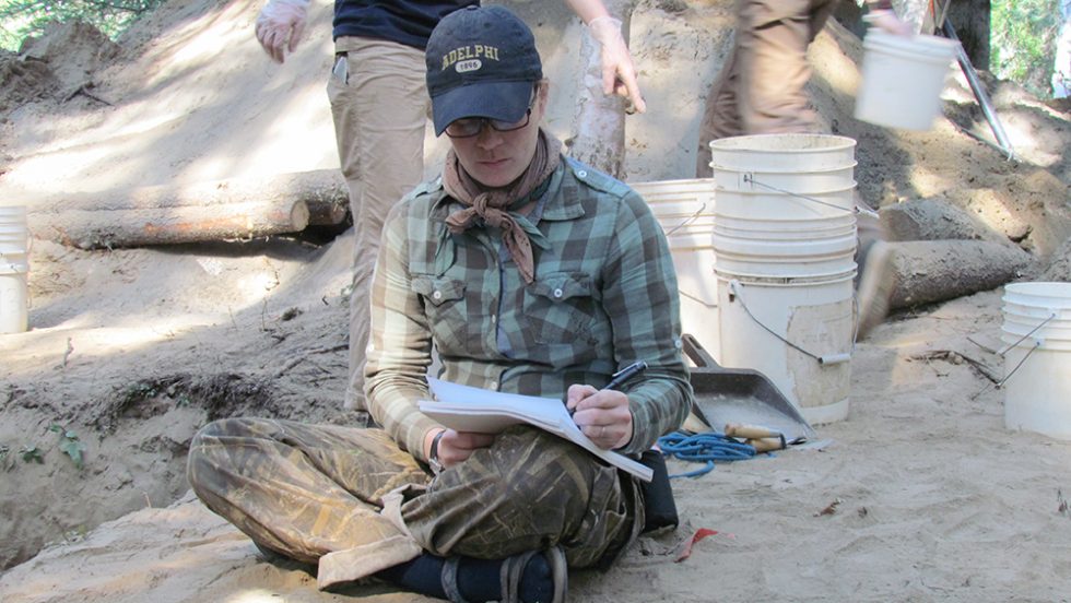 An Adelphi student writing notes during an archeological dig.