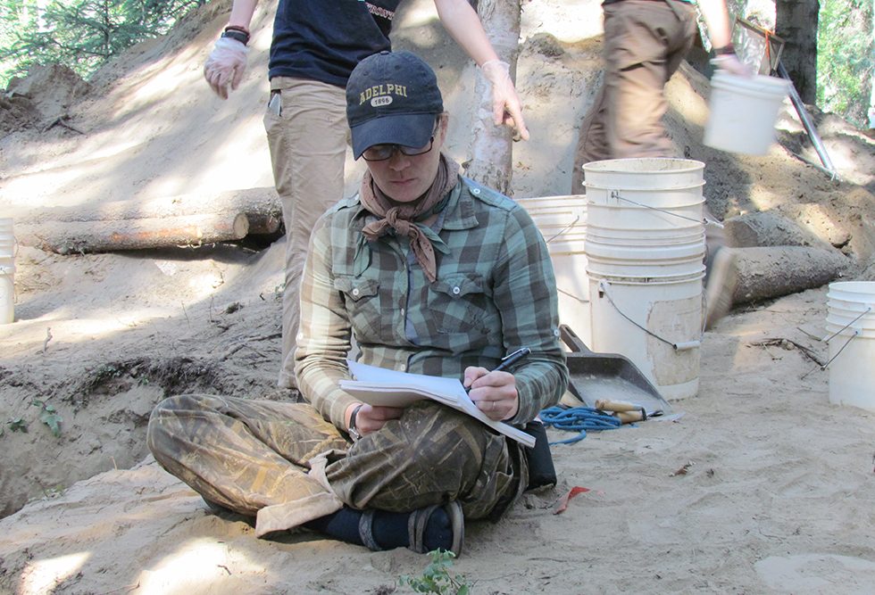 An Adelphi student writing notes during an archeological dig.