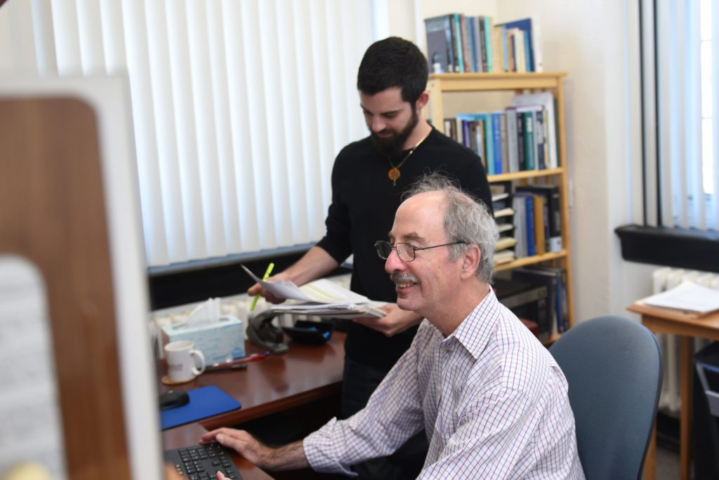 Professor Bornstein listening to a PhD psychology student explain a point in front of a computer with data showing on the screen.