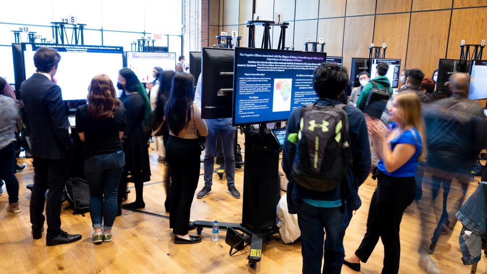 Participants walking around the conference floor where large poster screens are on display.