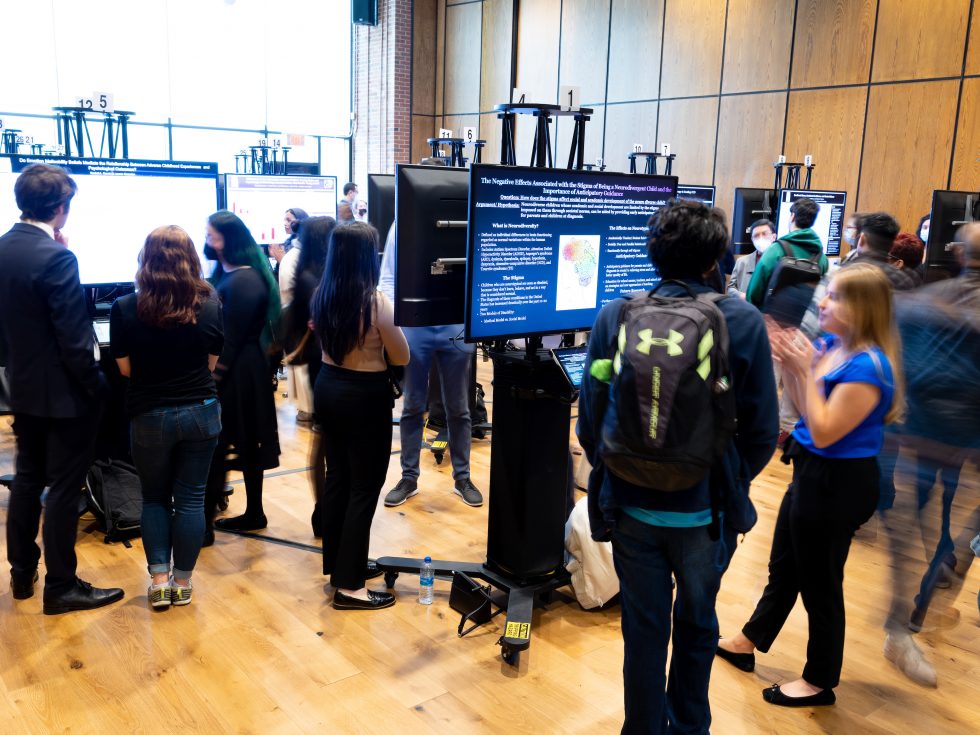 Participants walking around the conference floor where large poster screens are on display.