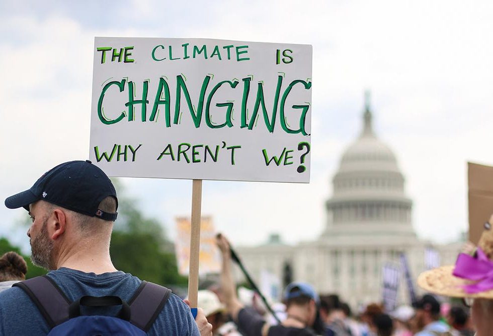 A man holding a sign that says "the climate is changing, why aren't we?"