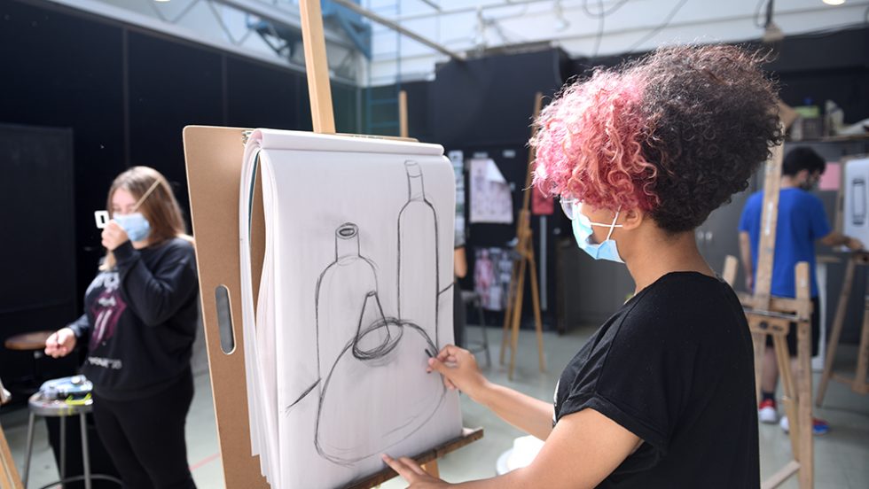 Students drawing charcoal still lifes during class while wearing masks to protect against the COVID-19 virus.