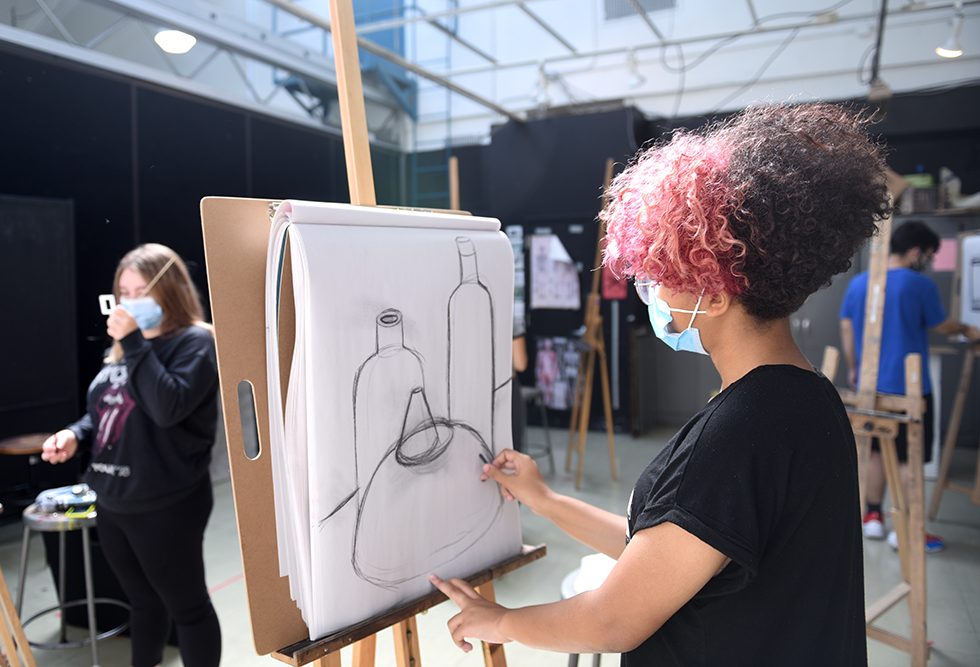 Students drawing charcoal still lifes during class while wearing masks to protect against the COVID-19 virus.