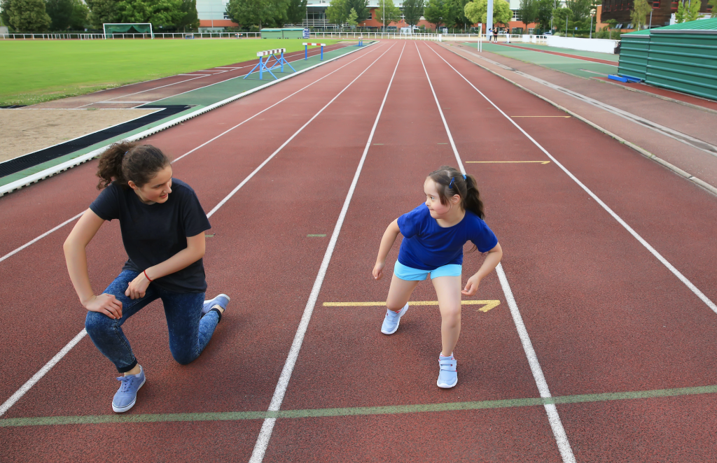 An instructor works with a young child on a track field. They are practicing the starting position one-on-one.