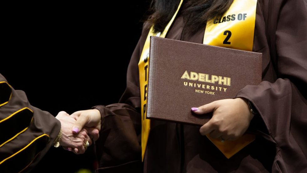 An Adelphi graduate shakes hands while holding her diploma.