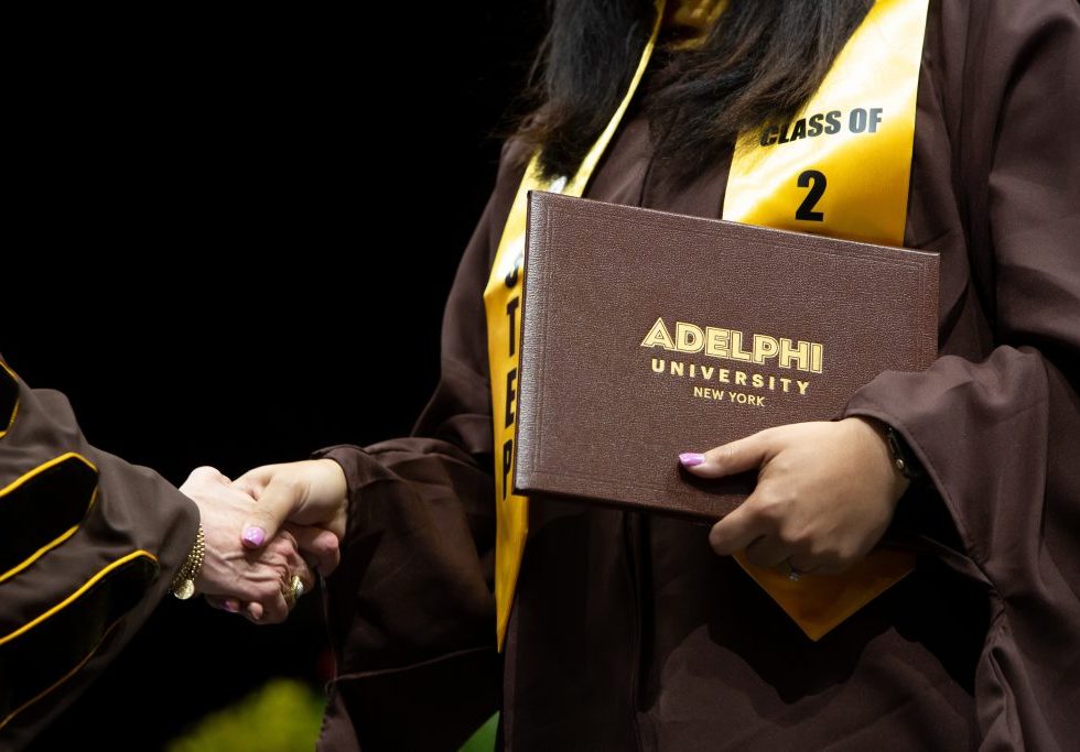 An Adelphi graduate shakes hands while holding her diploma.