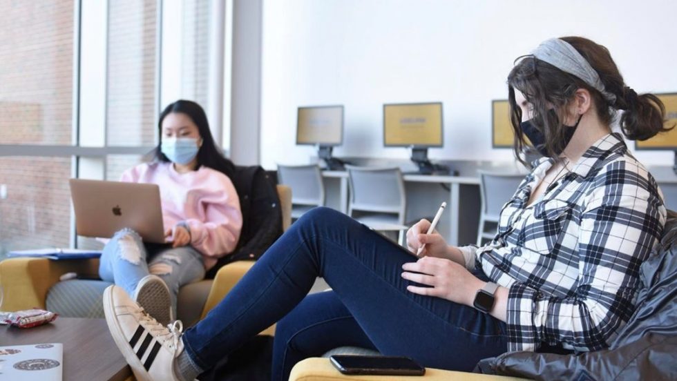 Adelphi students studying while wearing masks in a computer lab and lounge on campus.