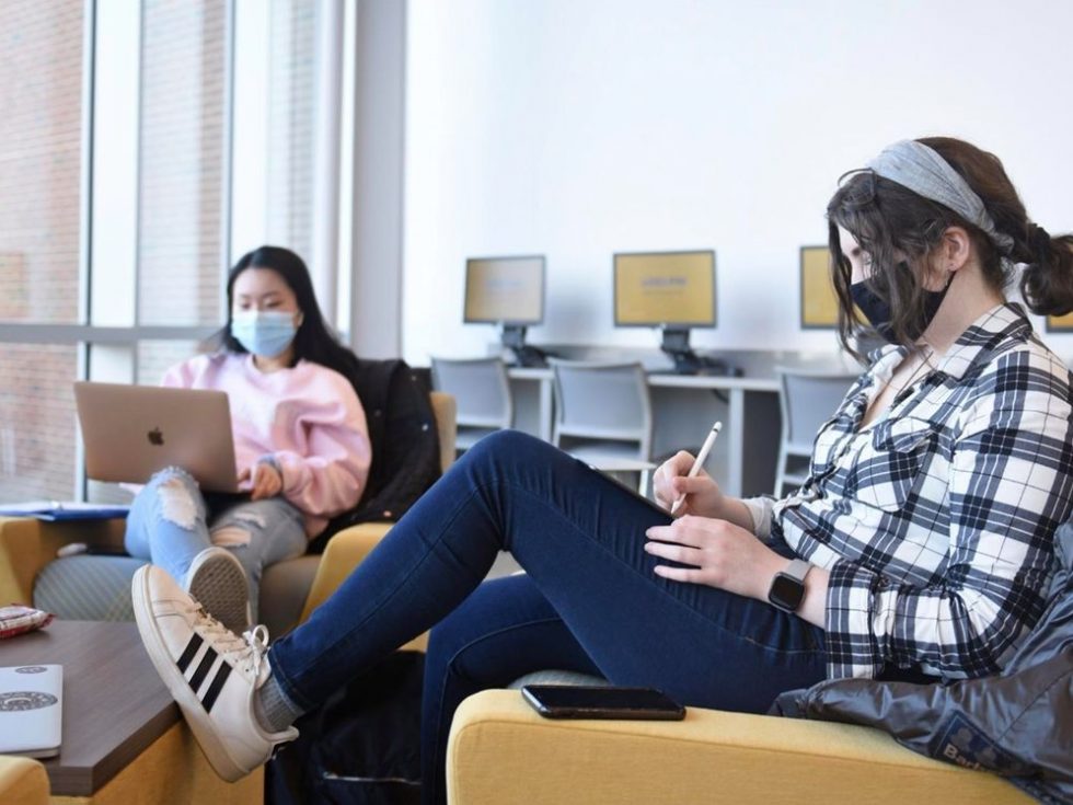 Adelphi students studying while wearing masks in a computer lab and lounge on campus.