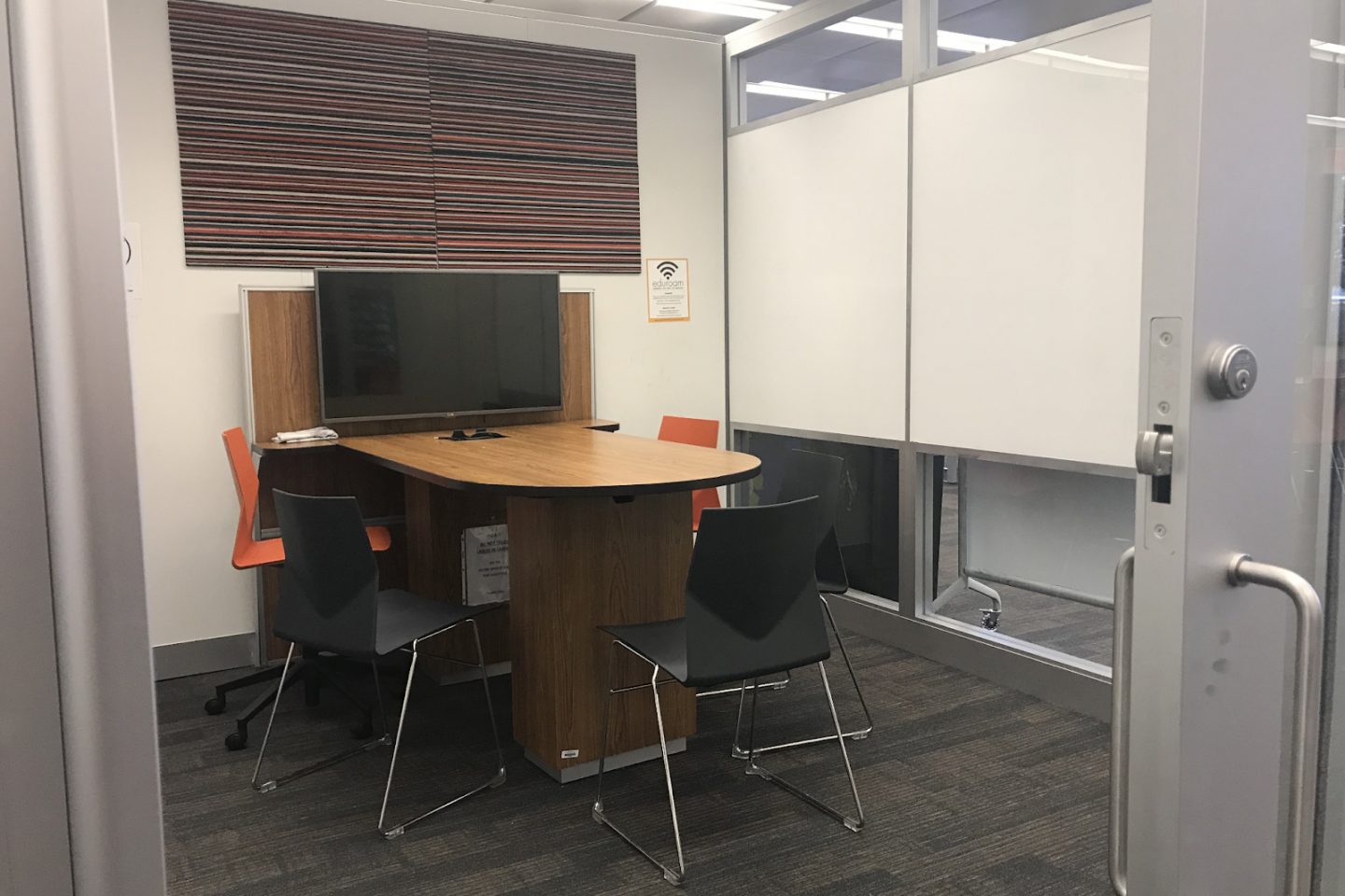 A peek inside a collaboration studio pod, showing a screen, deak and seating for group study