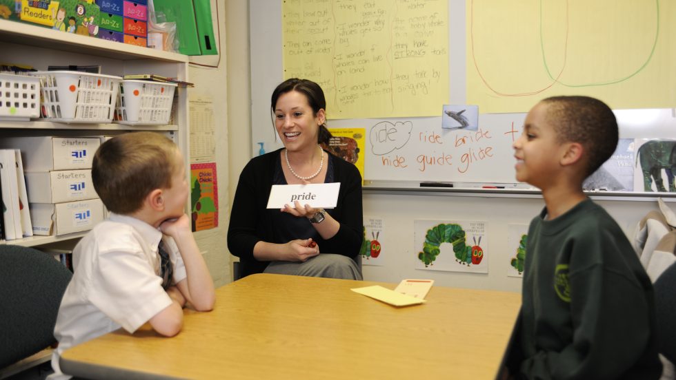 An Adelphi student working with two school aged children on reading and speech skills with flash cards.