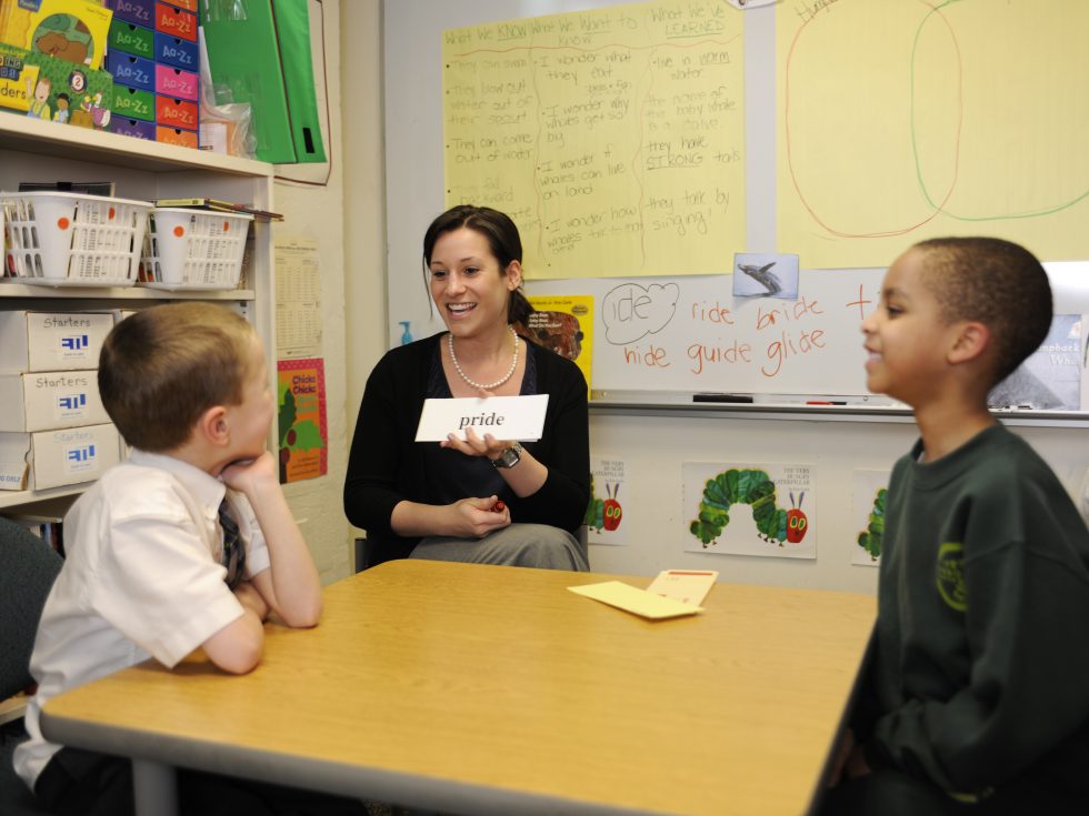 An Adelphi student working with two school aged children on reading and speech skills with flash cards.