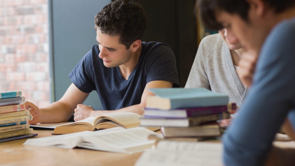 Students at a desk studying with books around.