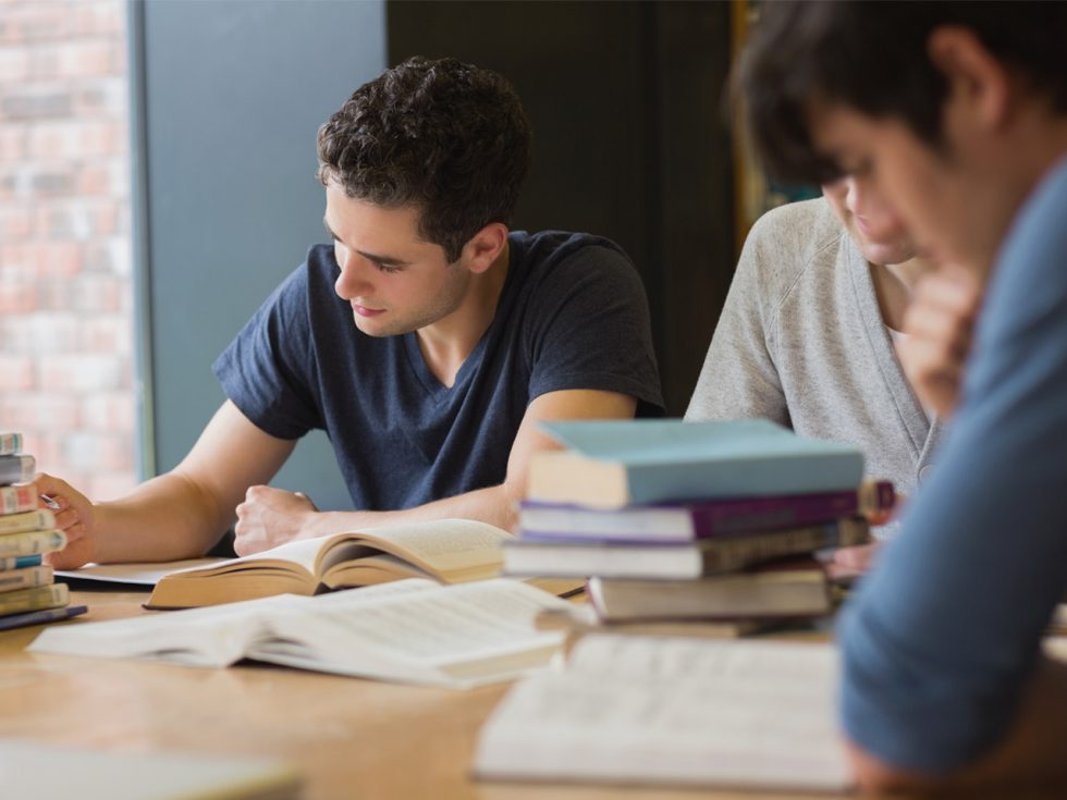 Students at a desk studying with books around.