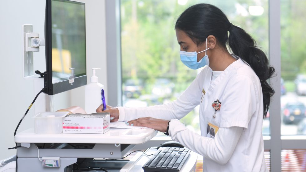 An Adelphi nursing student wearing a face-mask and working at a computer.