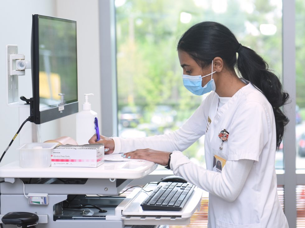 An Adelphi nursing student wearing a face-mask and working at a computer.
