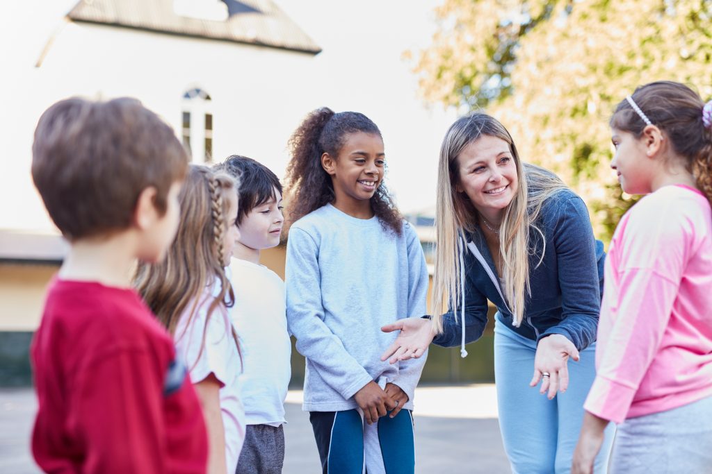 A Physical Education teacher talking with a group of young children.