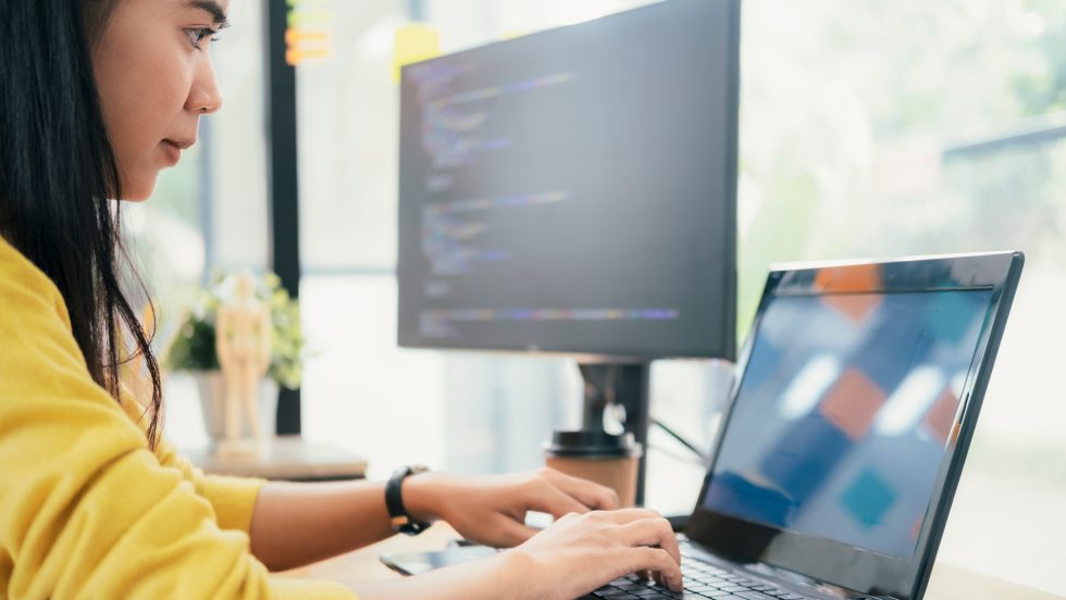 Programmer coding at her desk with a laptop and dual monitor