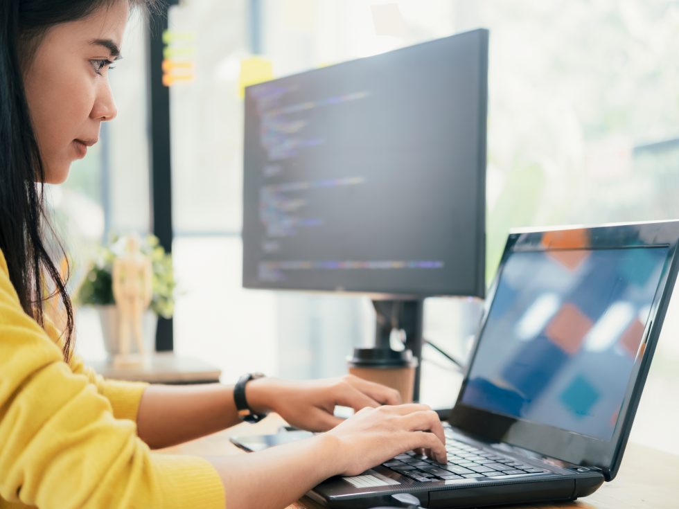 Programmer coding at her desk with a laptop and dual monitor