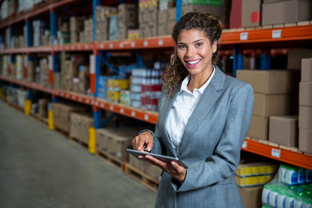 Supply chain professional woman standing in a warehouse using a tablet.
