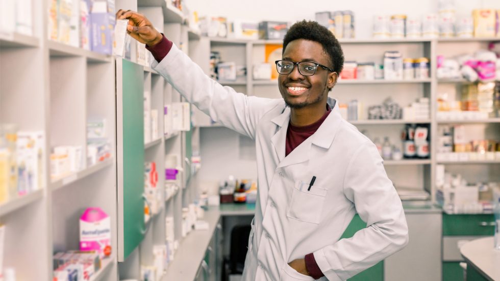 A young professional in a white lab-coat taking a medication off a shelf