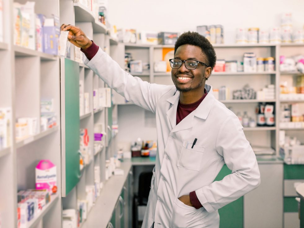 A young professional in a white lab-coat taking a medication off a shelf