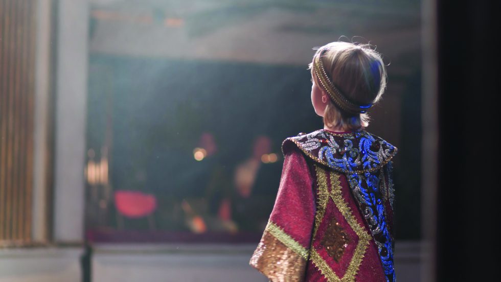 A small child on stage wearing a royal costume.