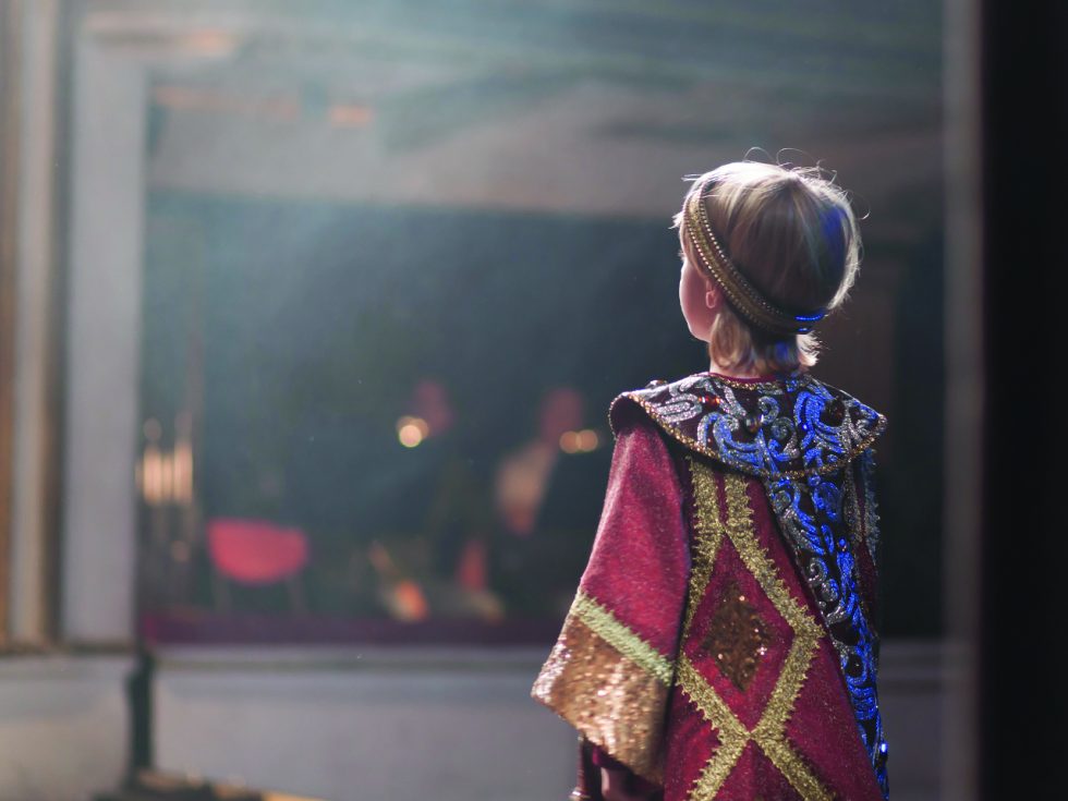 A small child on stage wearing a royal costume.