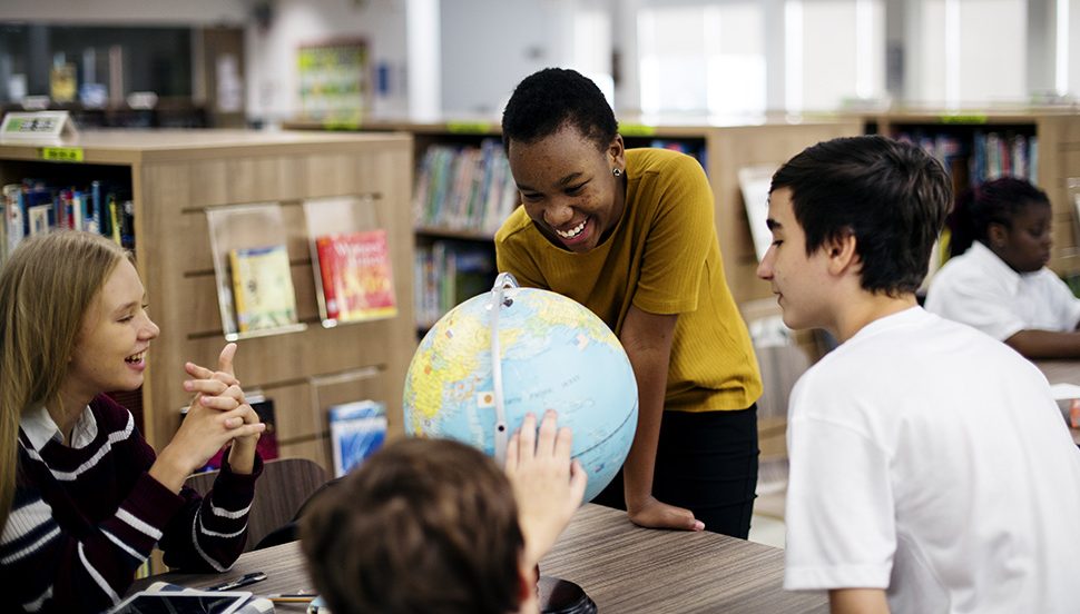 Students engaging and smiling in school with a globe.