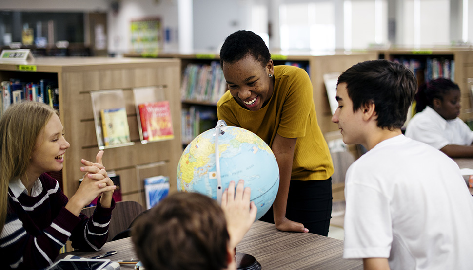 Students engaging and smiling in school with a globe.