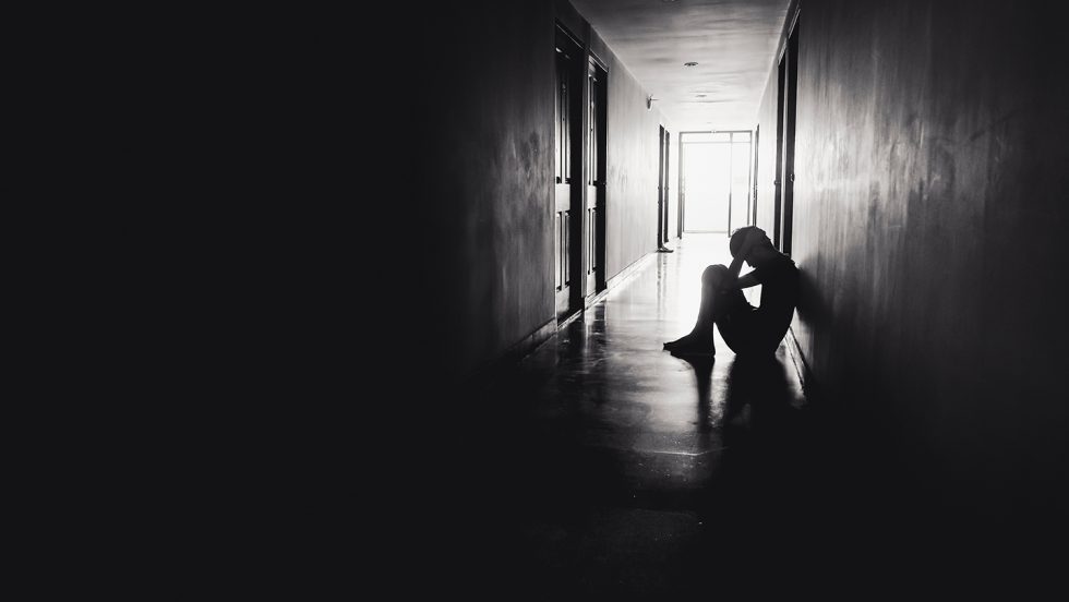 Depression concept: Person sitting on the floor in a dark hallway