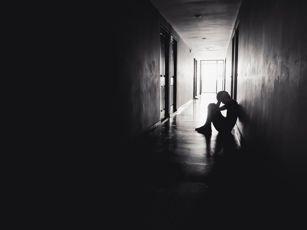 Depression concept: Person sitting on the floor in a dark hallway