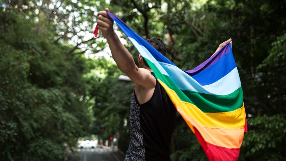 A person holding a rainbow pride flag over their back