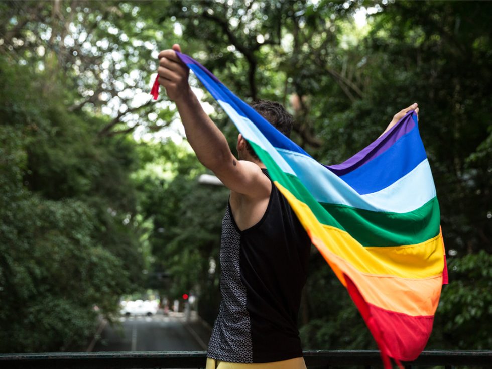 A person holding a rainbow pride flag over their back