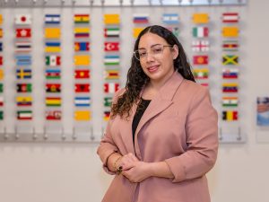 Carla Alvarez standing in front of a wall of international flags on Adelphi University's campus.