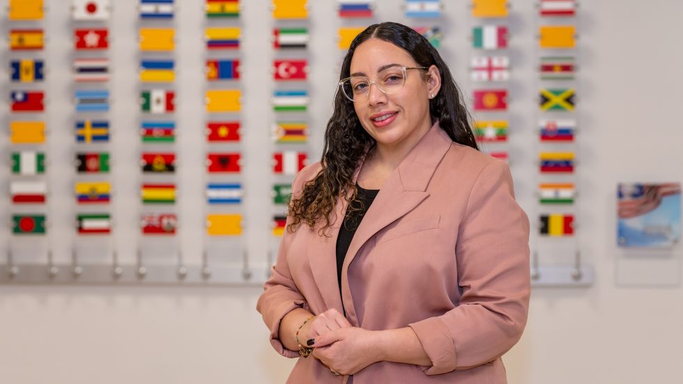 Carla Alvarez standing in front of a wall of international flags on Adelphi University's campus.