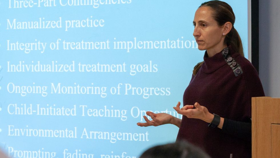 Dana Battaglia, PhD, standing in front of a slide presentation during a lecture.